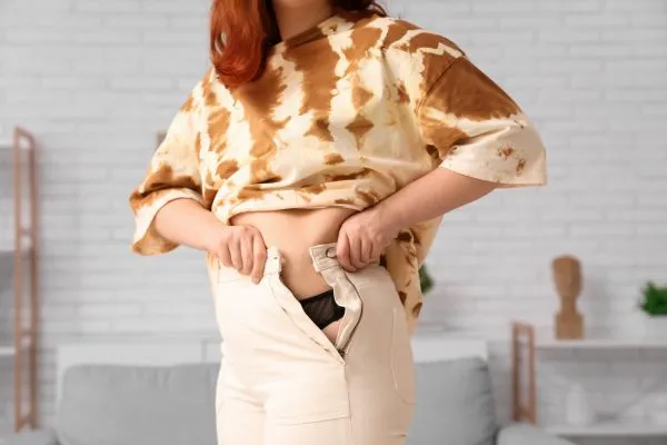 Image of woman trying to do her trousers up after pregnancy weight gain Keighley