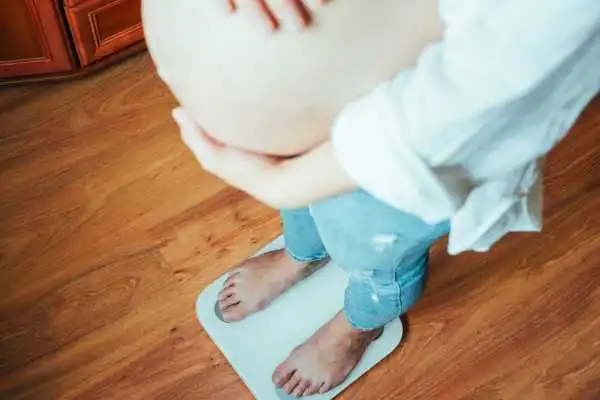 Image of woman weighing herself and experiencing weight gain through pregnancy Keighley
